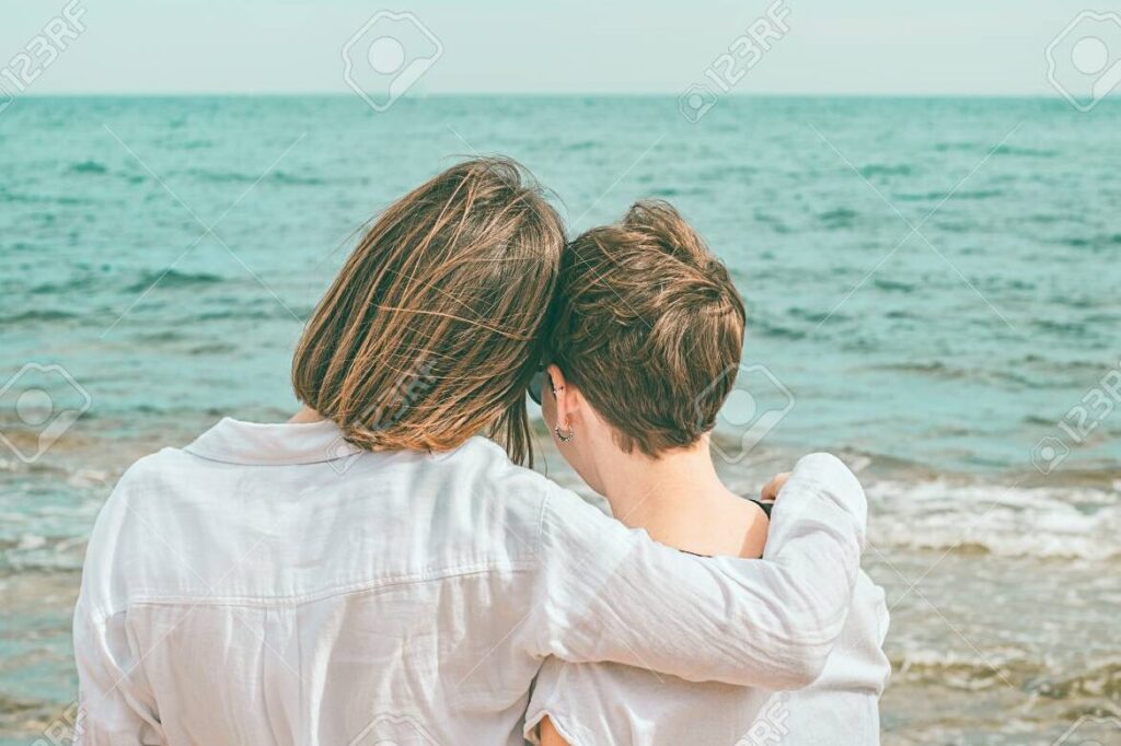 dos mujeres sonriendo y abrazandose en la playa al atardecer