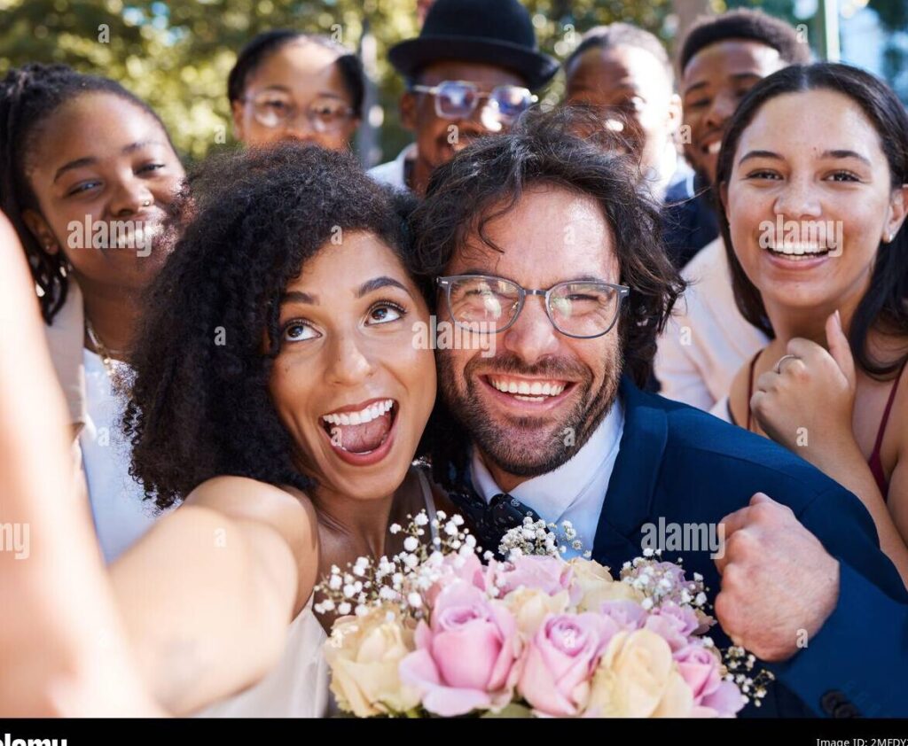 imagen de una pareja de novios sonriendo y abrazandose en su boda rodeados de amigos y familiares felices