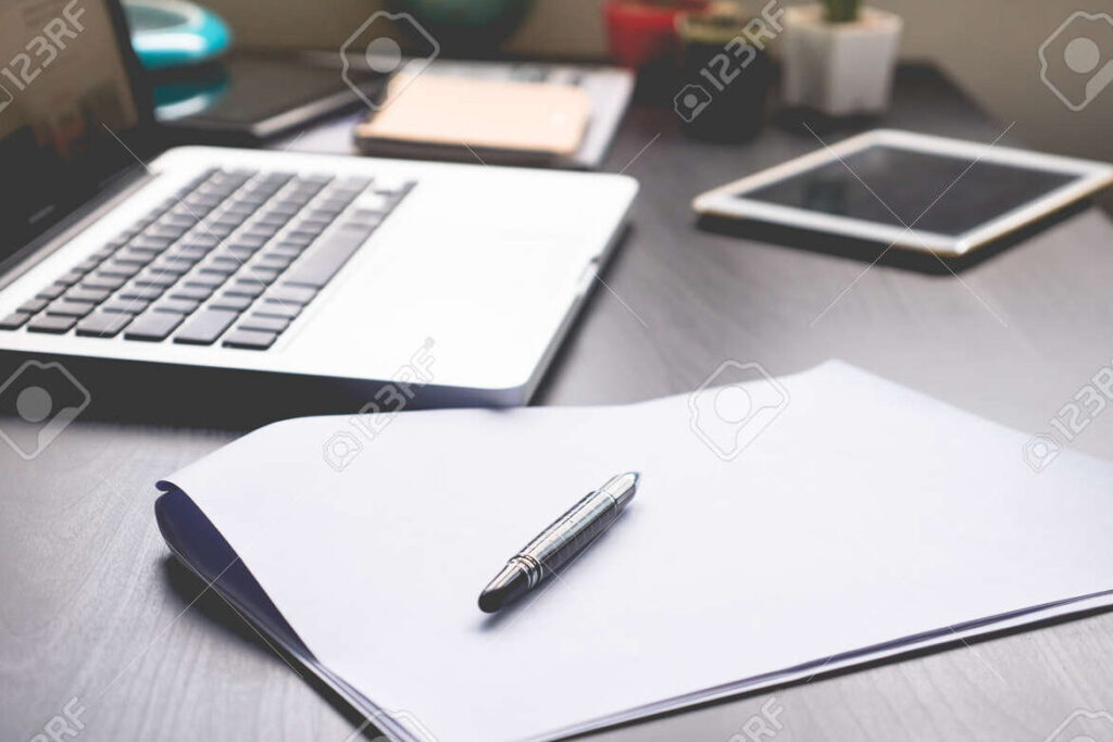 un escritorio con una computadora una pluma y un papel en blanco
