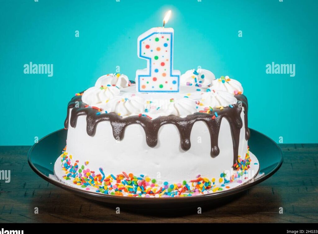 una foto de un pastel de cumpleanos decorado con colores brillantes y una vela encendida en forma de numero uno