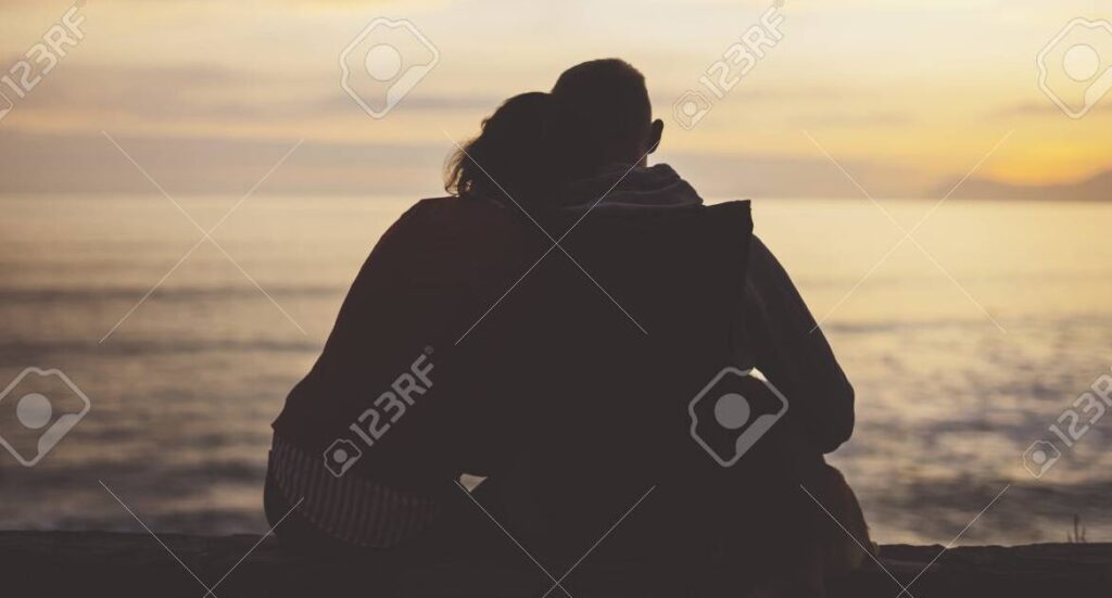 una imagen de dos personas abrazadas mirando el atardecer en la playa