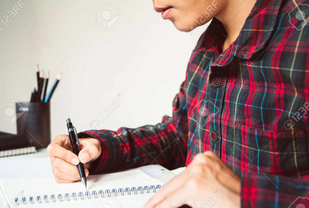 una imagen de un estudiante escribiendo una carta en un escritorio con un boligrafo y papel