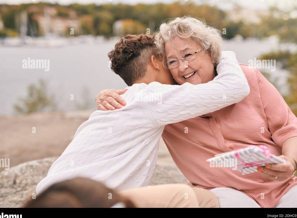 una imagen de una abuela sonriente abrazando a su nieto mientras reciben un regalo
