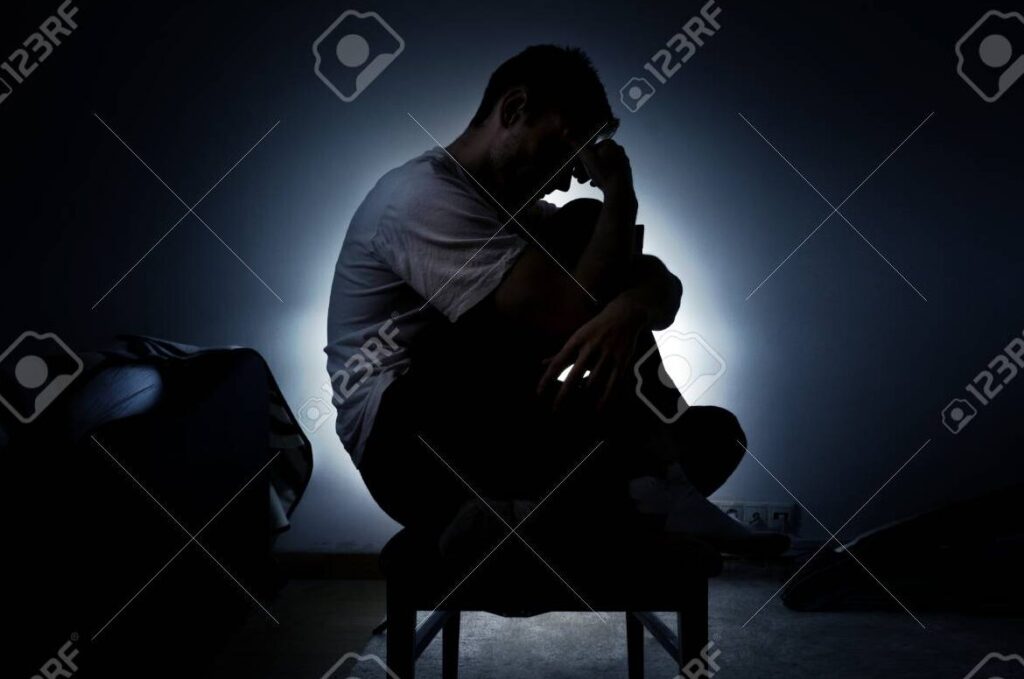 una imagen en blanco y negro de una persona solitaria sentada en un banco con la cabeza gacha y expresion triste