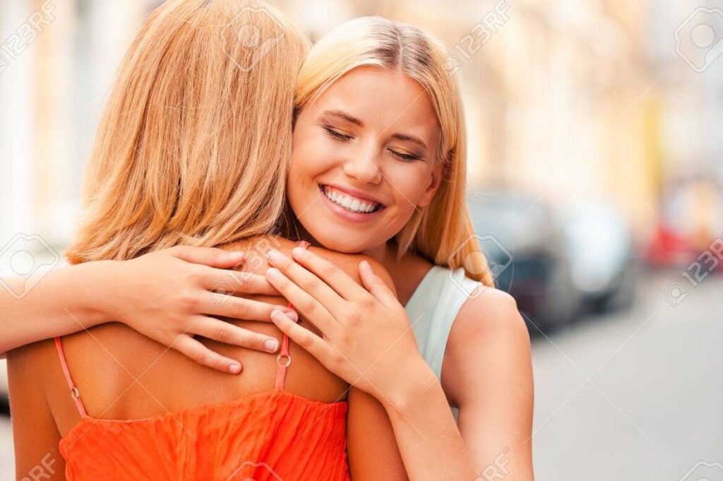 una madre sonriendo y abrazando a su hija mientras ella se aleja