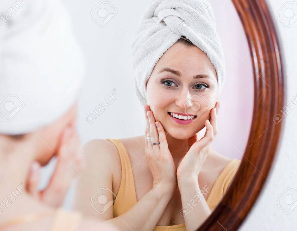 una mujer de pie frente a un espejo mirandose con confianza y sonriendo