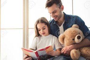 una nina sonriendo mientras su padre le lee un libro