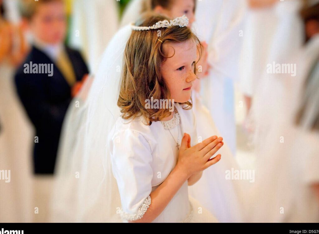 una nina sonriente vestida de blanco sosteniendo una vela de la primera comunion