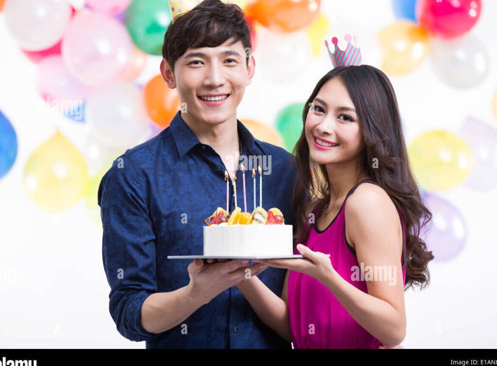 una pareja sonriente celebrando su aniversario con un pastel y globos