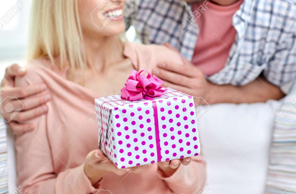 una pareja sonriente sosteniendo una caja de regalo envuelta en papel de colores