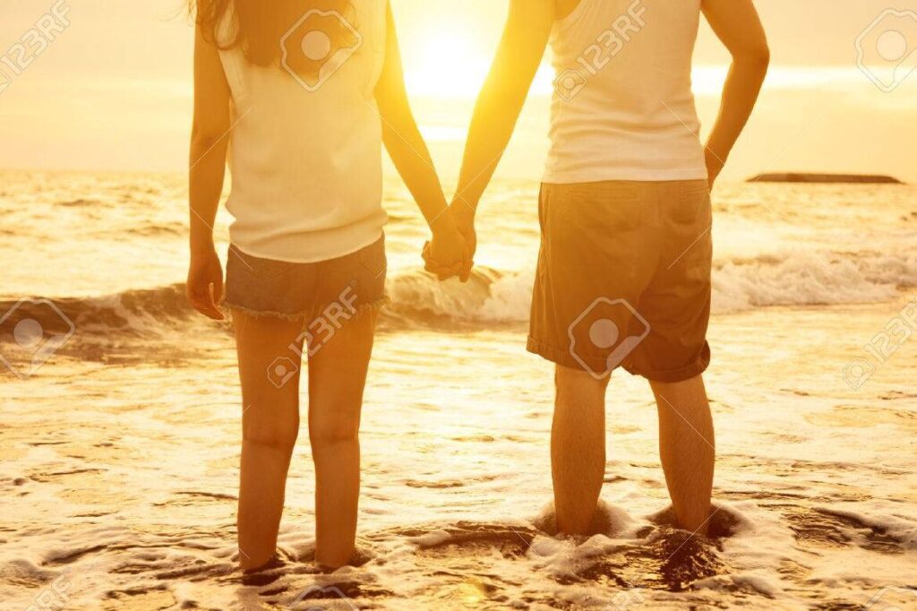 una pareja tomada de la mano en un atardecer en la playa