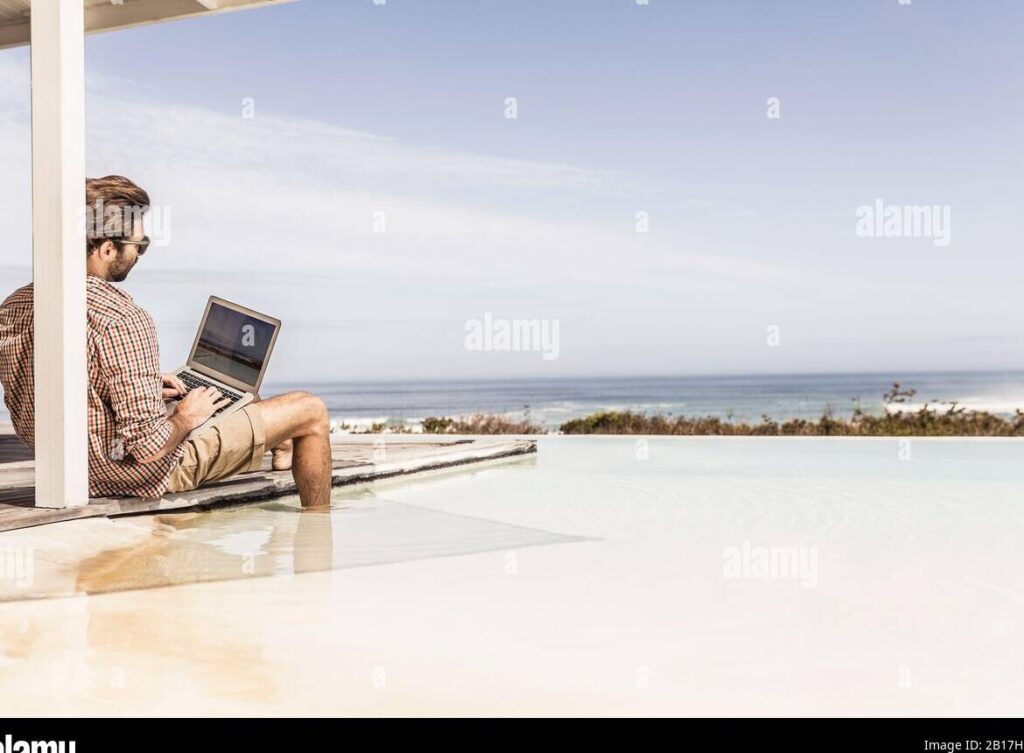 una persona en la playa con una sombrilla y una laptop cerrada a su lado