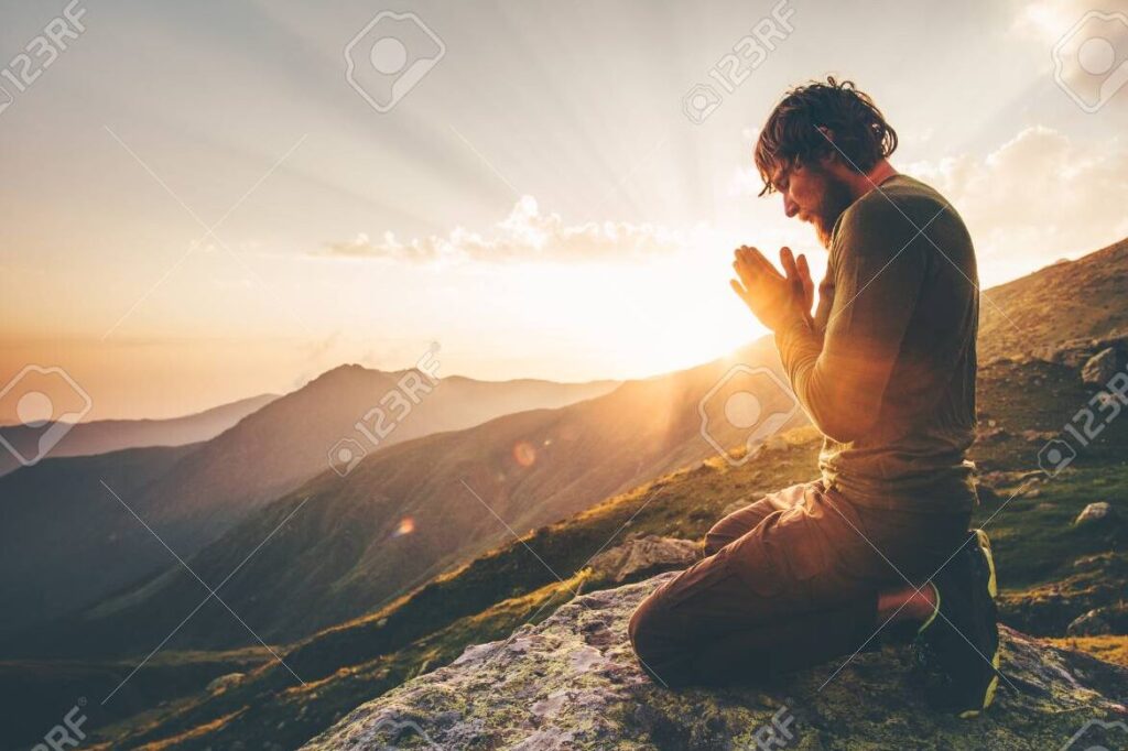 una persona rezando en un paisaje de montanas al atardecer