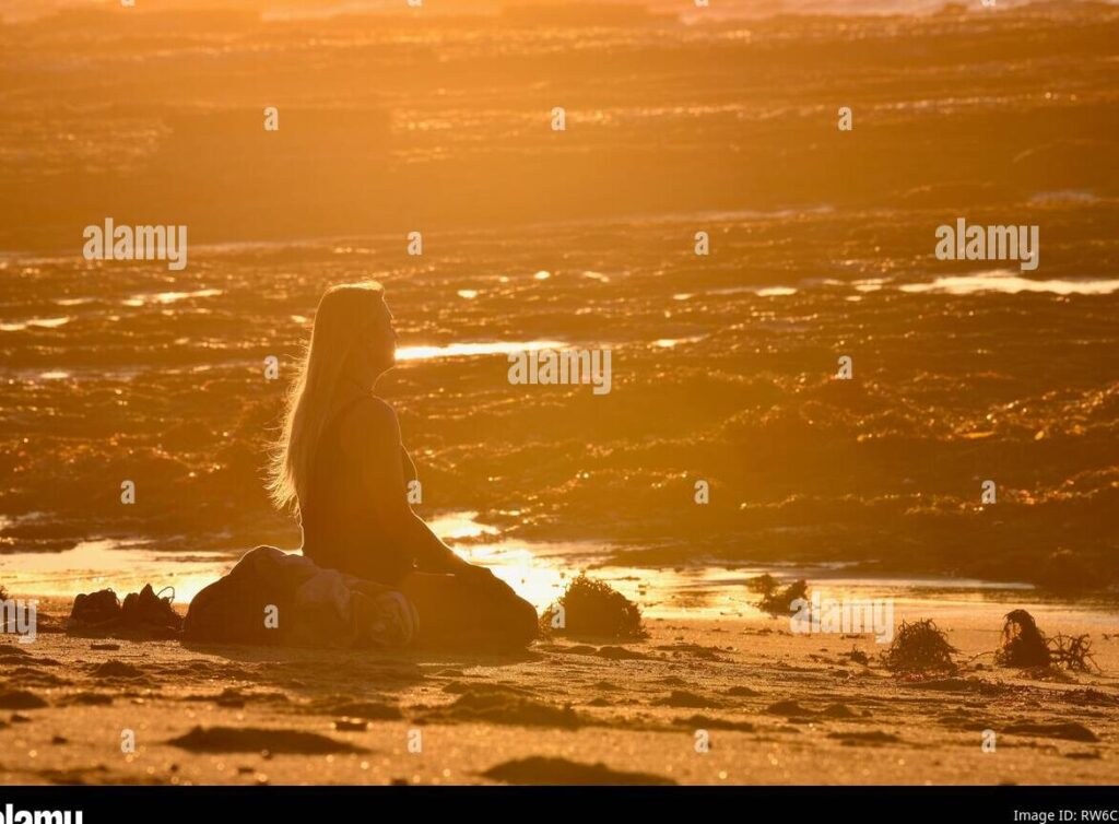 una persona sentada en posicion de meditacion frente a un paisaje tranquilo con colores calidos al atardecer